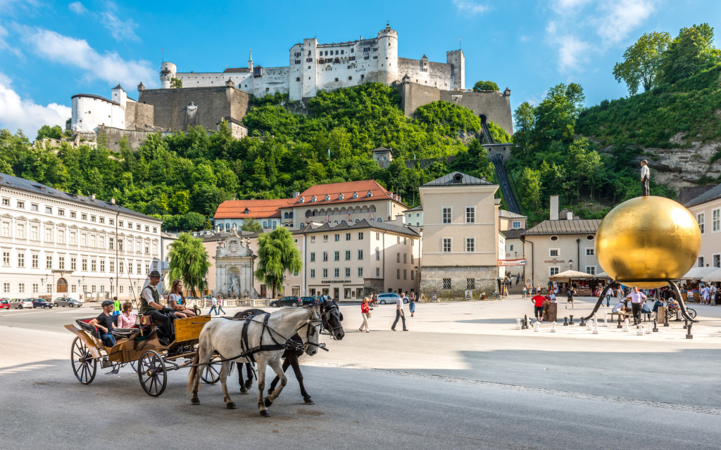Pferdekutsche auf dem Kapitelplatz vor historischen Gebäuden und einer Burg auf bewaldetem Hügel